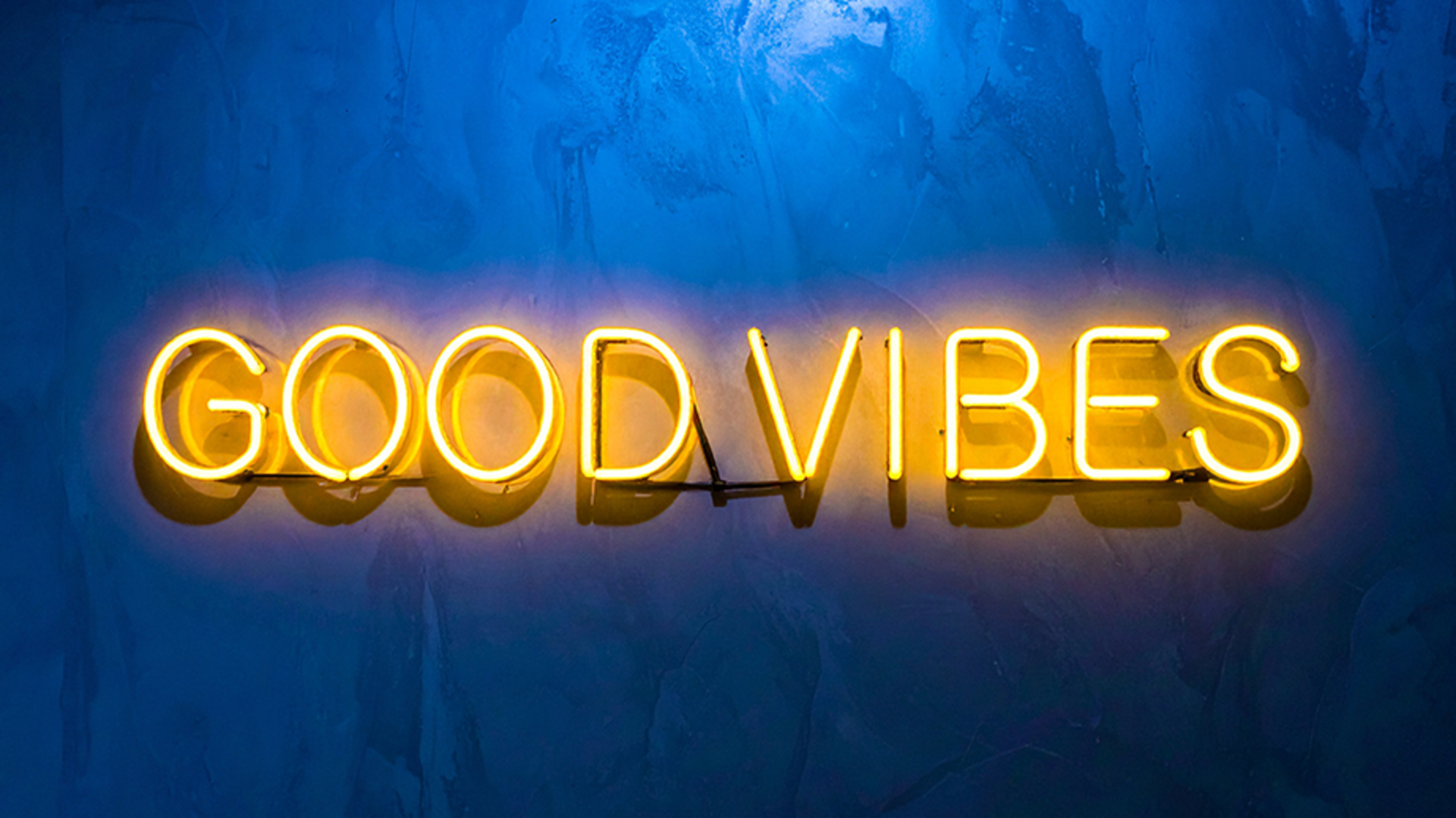 Gelbe Neonröhren mit dem Spruch 'Good Vibes' an einer leicht bläulichen, glatten Wand